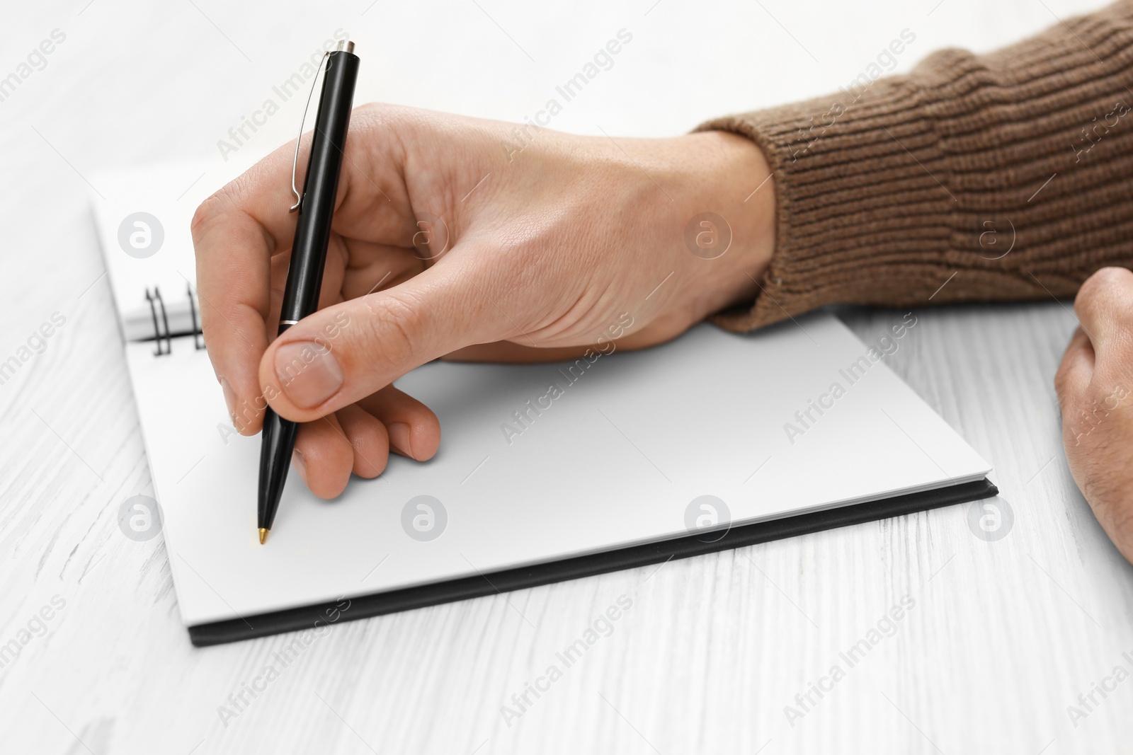 Photo of Man writing in notebook at white wooden table, closeup