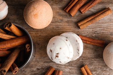 Photo of Bath bombs with cinnamon sticks on wooden table, top view