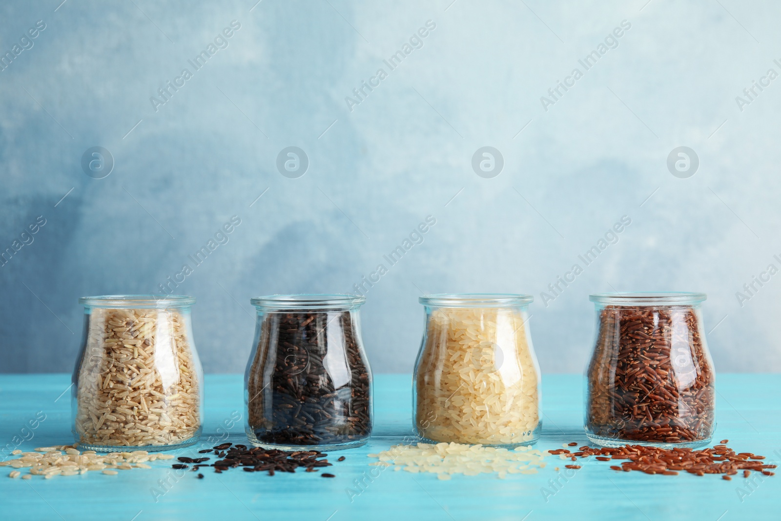 Photo of Jars with different types of rice on blue table