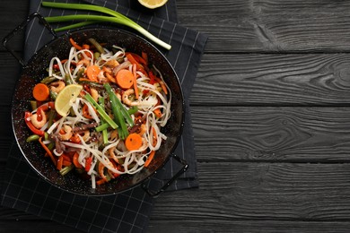 Photo of Shrimp stir fry with noodles and vegetables in wok on black wooden table, top view. Space for text