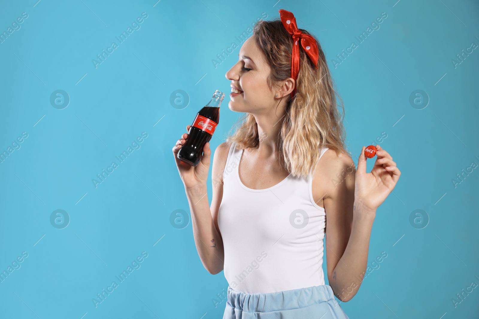 Photo of MYKOLAIV, UKRAINE - NOVEMBER 28, 2018: Young woman with bottle of Coca-Cola and cap on color background