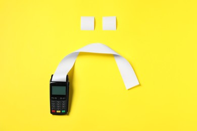 Photo of Payment terminal and sad face made of thermal paper for receipt on yellow background, flat lay