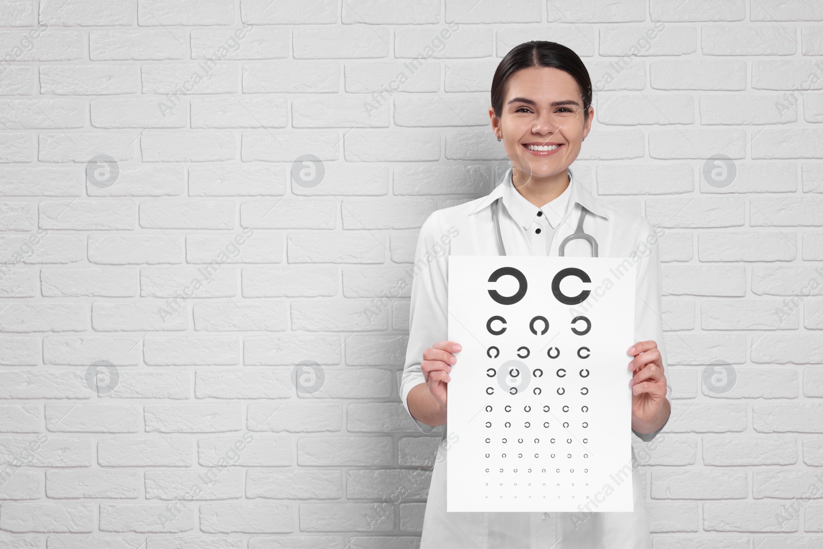 Photo of Ophthalmologist with vision test chart near white brick wall, space for text