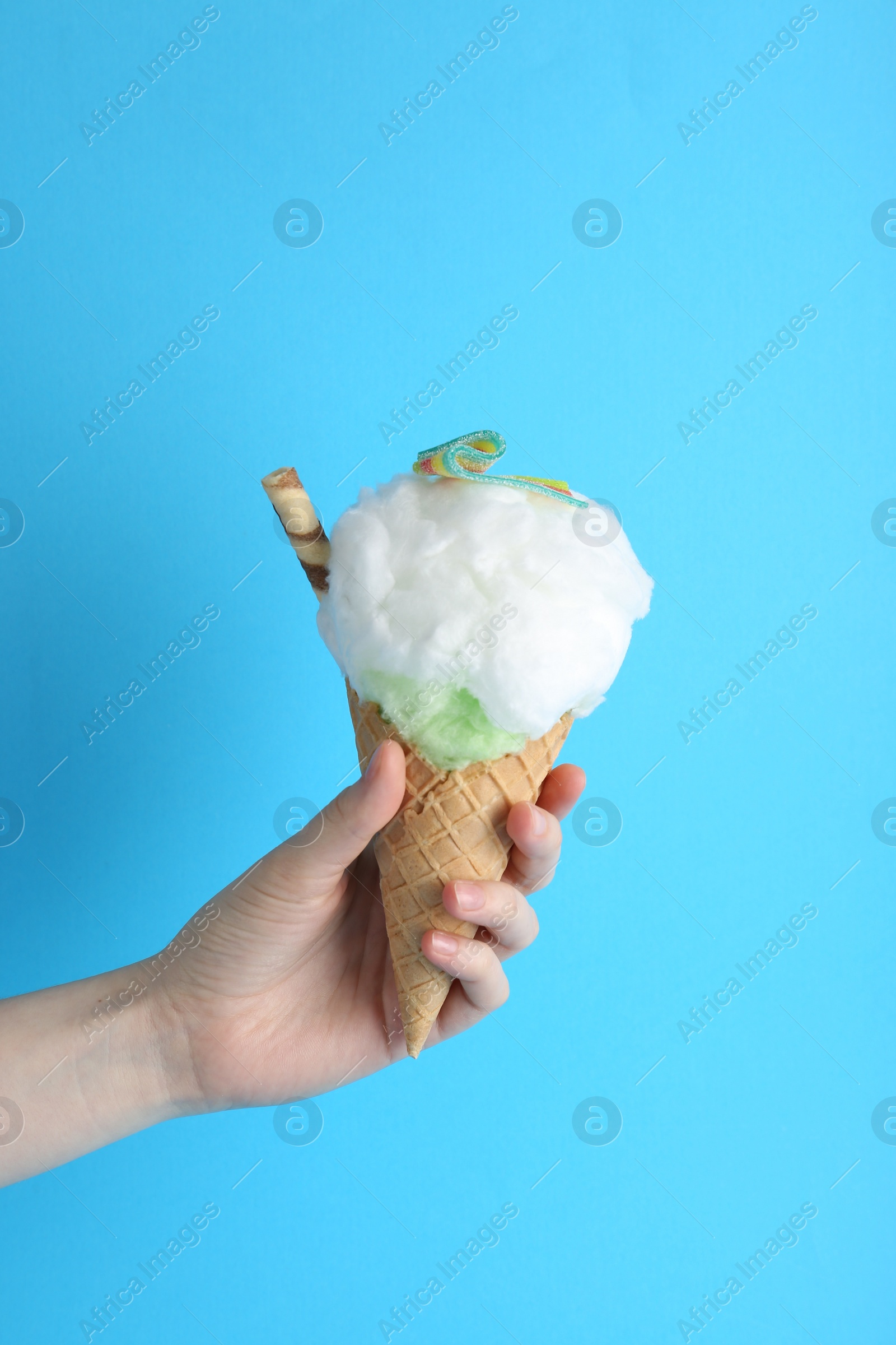 Photo of Woman holding waffle cone with cotton candy on light blue background, closeup