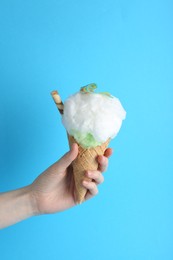 Woman holding waffle cone with cotton candy on light blue background, closeup