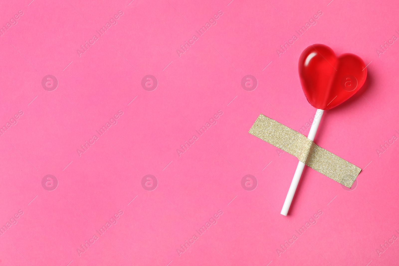 Photo of Sweet heart shaped lollipop taped to pink background, top view with space for text. Valentine's day celebration