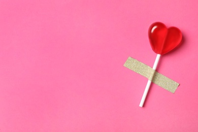 Photo of Sweet heart shaped lollipop taped to pink background, top view with space for text. Valentine's day celebration