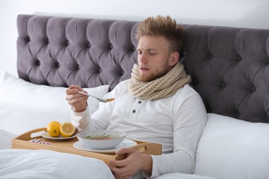 Sick young man eating soup to cure flu in bed at home
