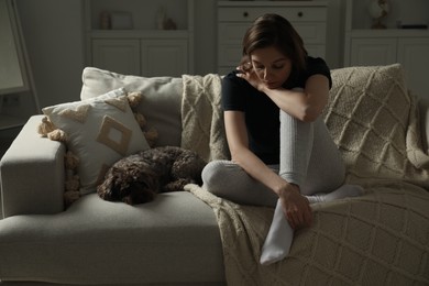 Photo of Sad young woman and her dog on sofa at home