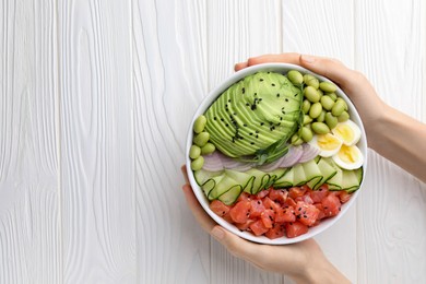 Photo of WOman holding delicious poke bowl with avocado, fish and edamame beans at white wooden table, top view. Space for text