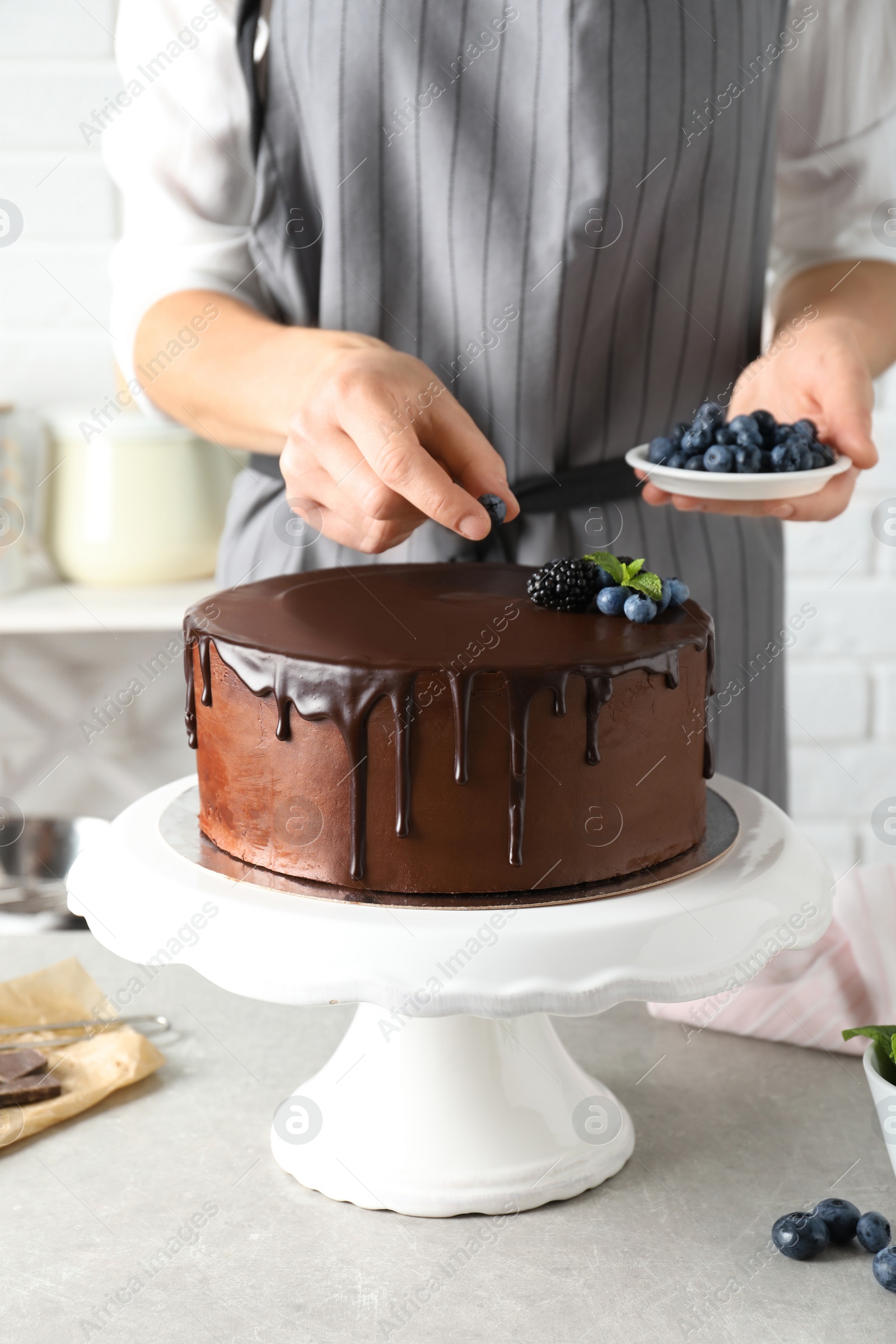 Photo of Baker decorating fresh delicious homemade chocolate cake with berries on table, closeup