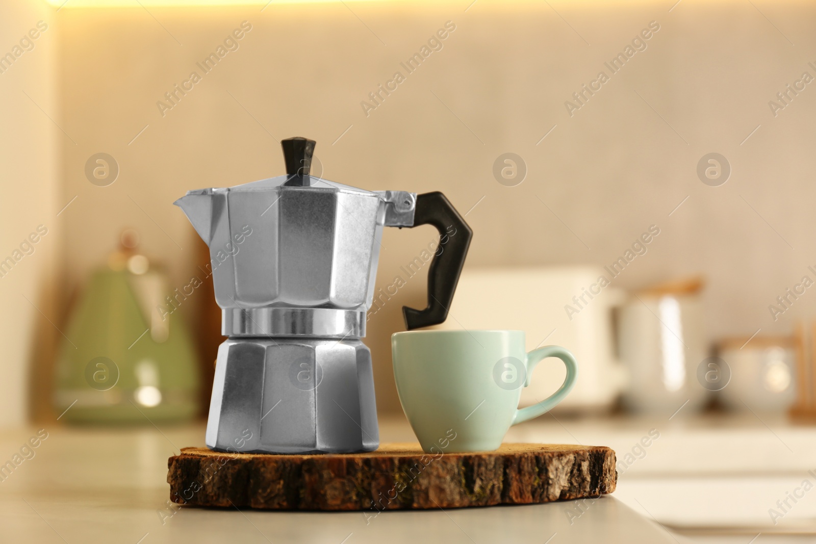 Photo of Cup of coffee and moka pot on light table in kitchen