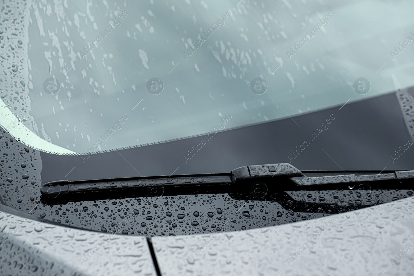 Photo of Car wiper cleaning water drops from windshield glass, closeup