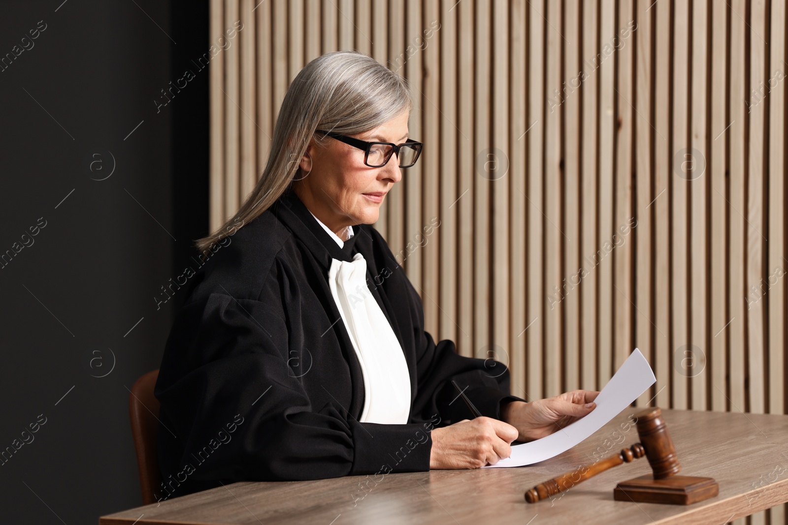 Photo of Judge in court dress working with document indoors