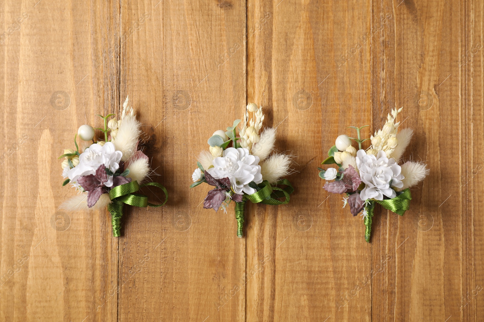 Photo of Stylish boutonnieres on wooden table, flat lay