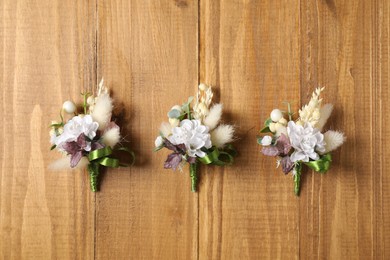 Stylish boutonnieres on wooden table, flat lay