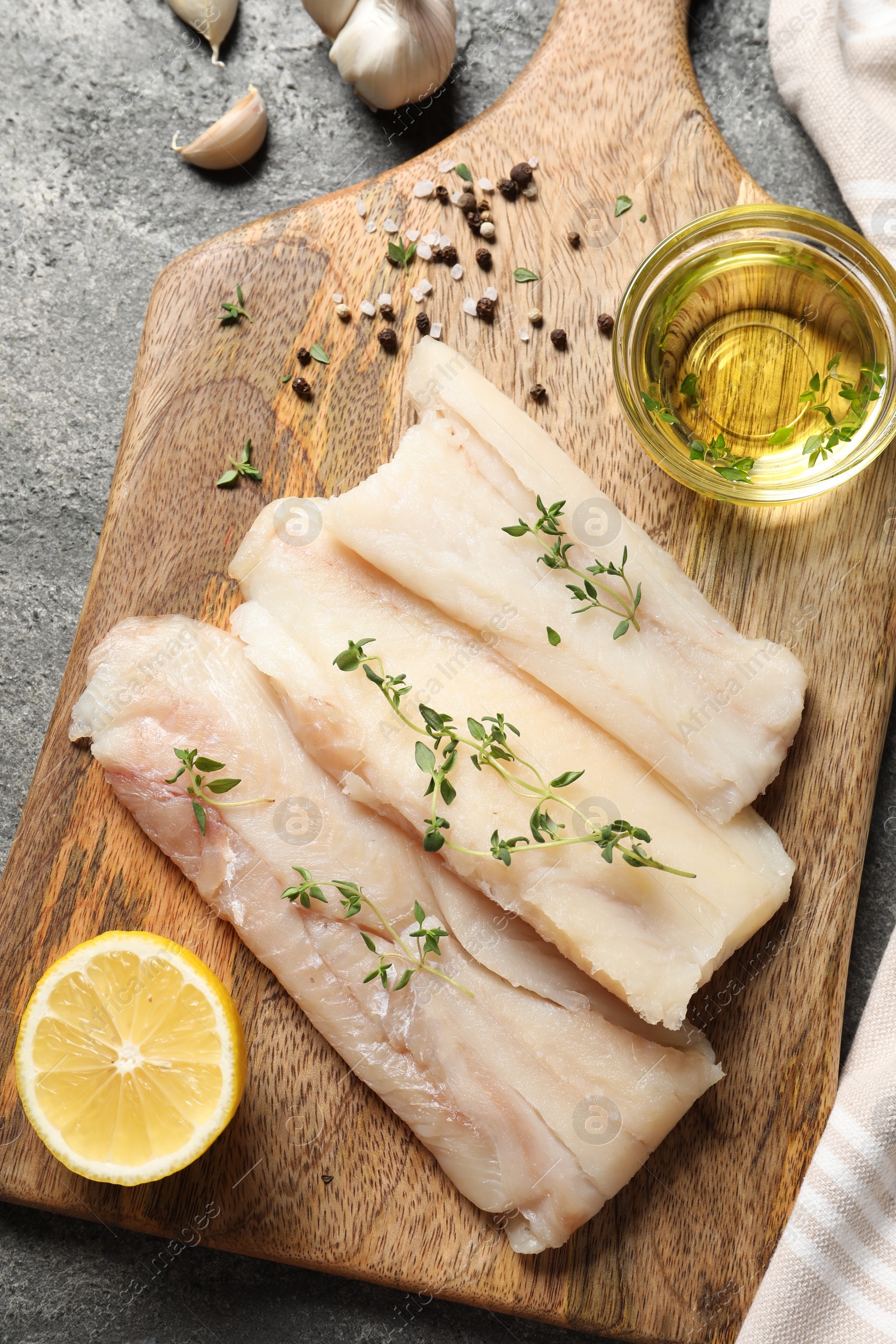 Photo of Raw cod fish, microgreens, oil, spices and lemon on grey textured table, top view