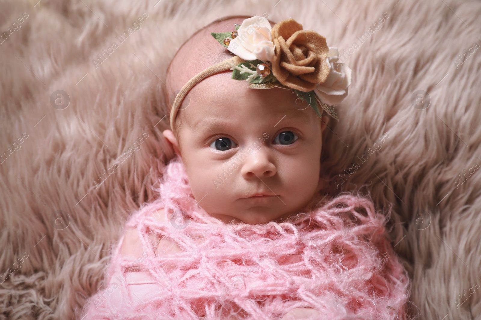 Photo of Cute newborn baby girl with floral headband lying on fuzzy rug, top view