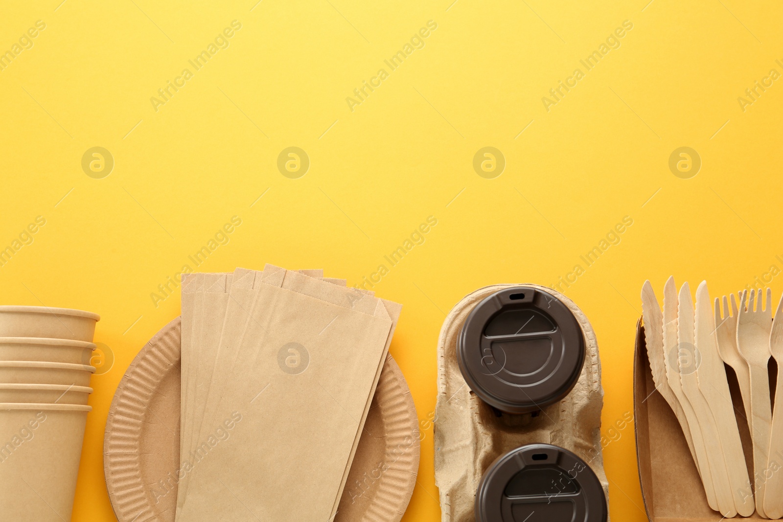 Photo of Flat lay of paper and wooden tableware on yellow background, space for text. Eco friendly lifestyle
