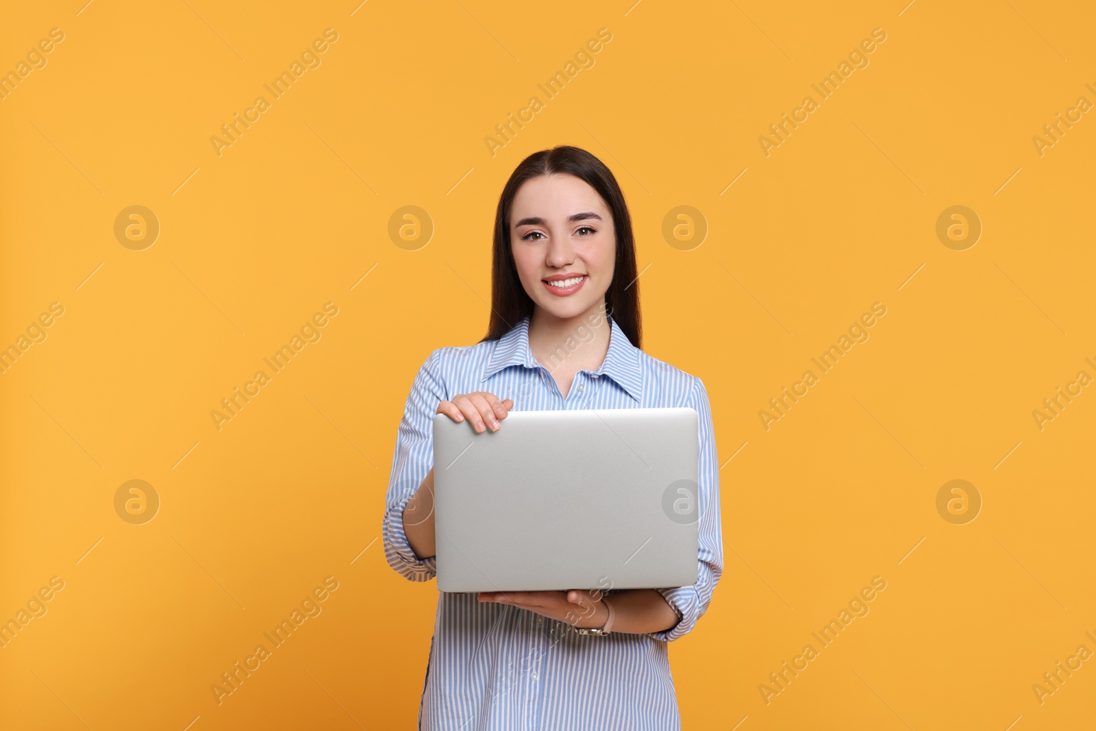 Photo of Smiling young woman with laptop on yellow background