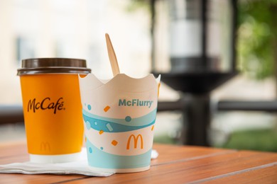 Photo of WARSAW, POLAND - SEPTEMBER 04, 2022: McDonald's hot drink and ice cream on wooden table outdoors, space for text