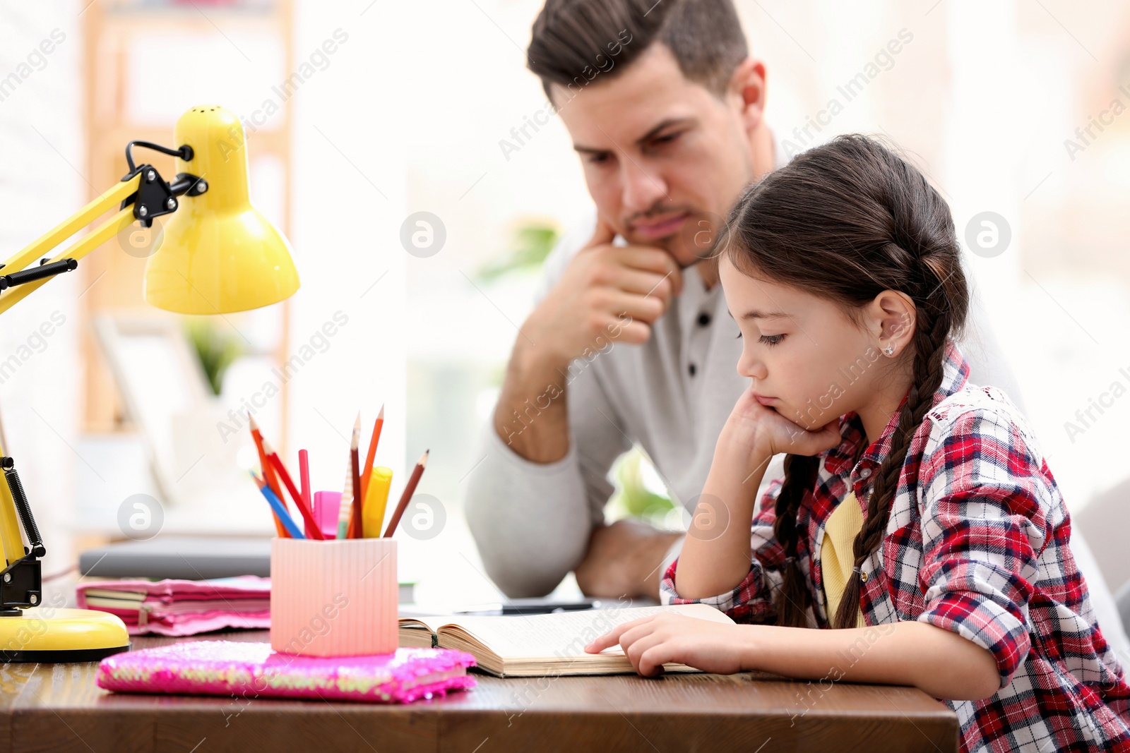 Photo of Man helping his daughter with homework at table indoors