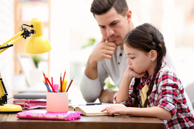 Man helping his daughter with homework at table indoors