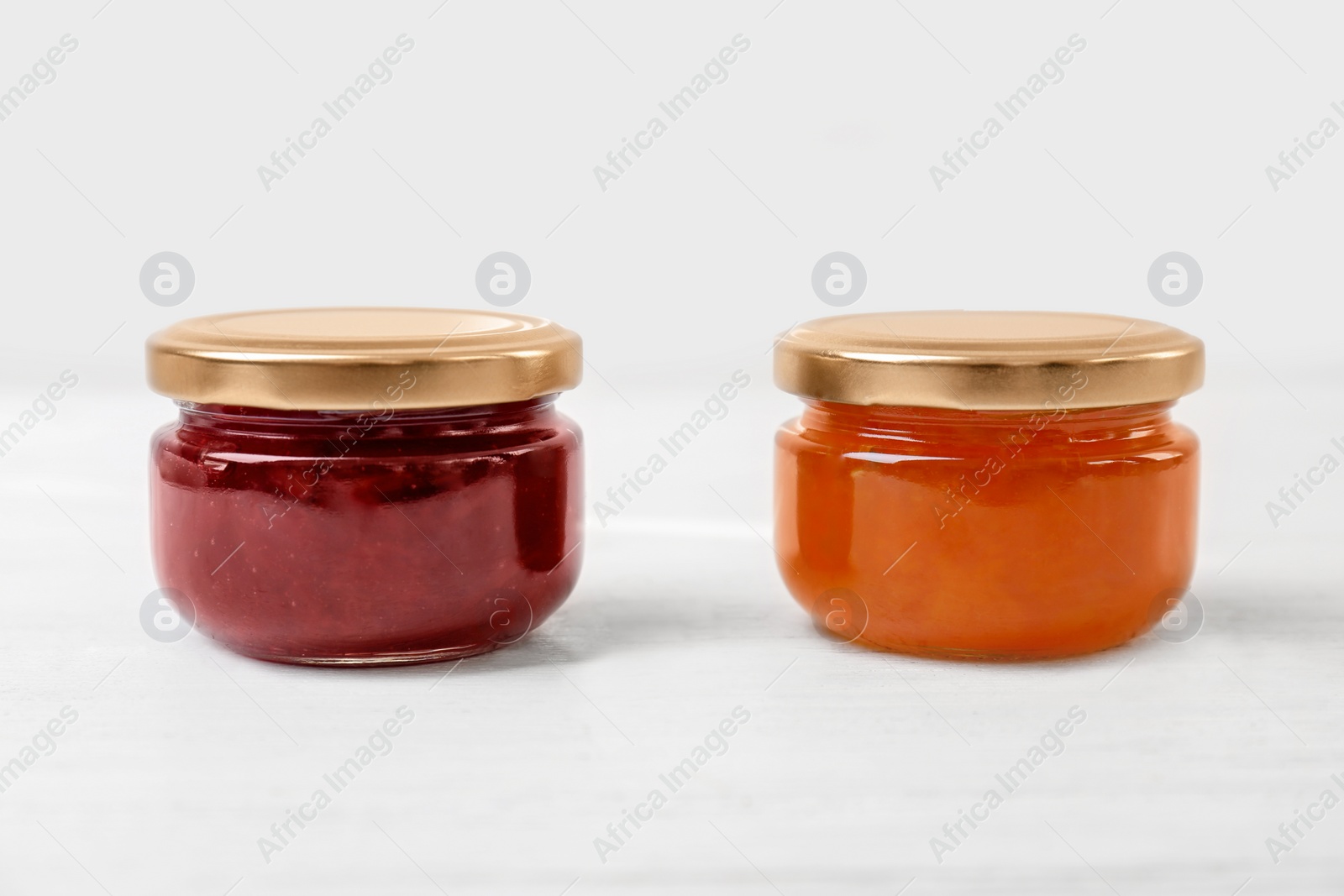 Photo of Two jars with tasty sweet jam on white wooden table