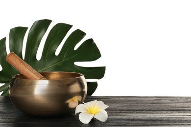 Photo of Golden singing bowl, mallet, green leaf and flower on wooden table against white background, space for text