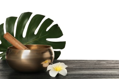 Golden singing bowl, mallet, green leaf and flower on wooden table against white background, space for text