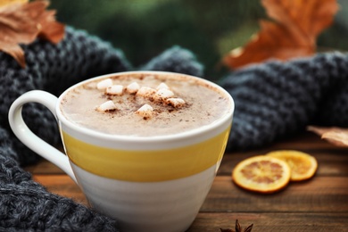 Cup of hot drink and scarf on window sill indoors, closeup. Cozy autumn atmosphere