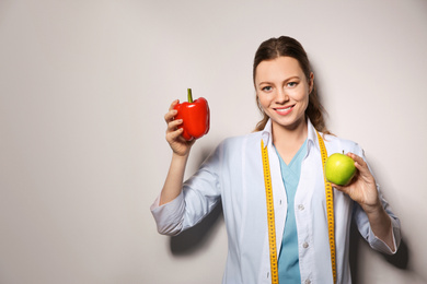 Photo of Nutritionist with bell pepper and apple on light grey background. Space for text