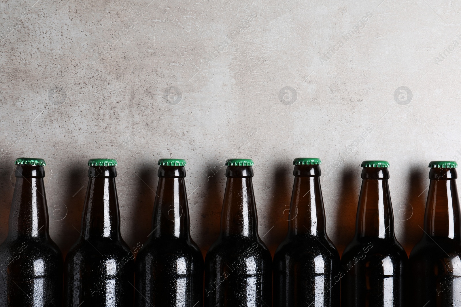 Photo of Glass bottles of beer on light grey background, flat lay. Space for text