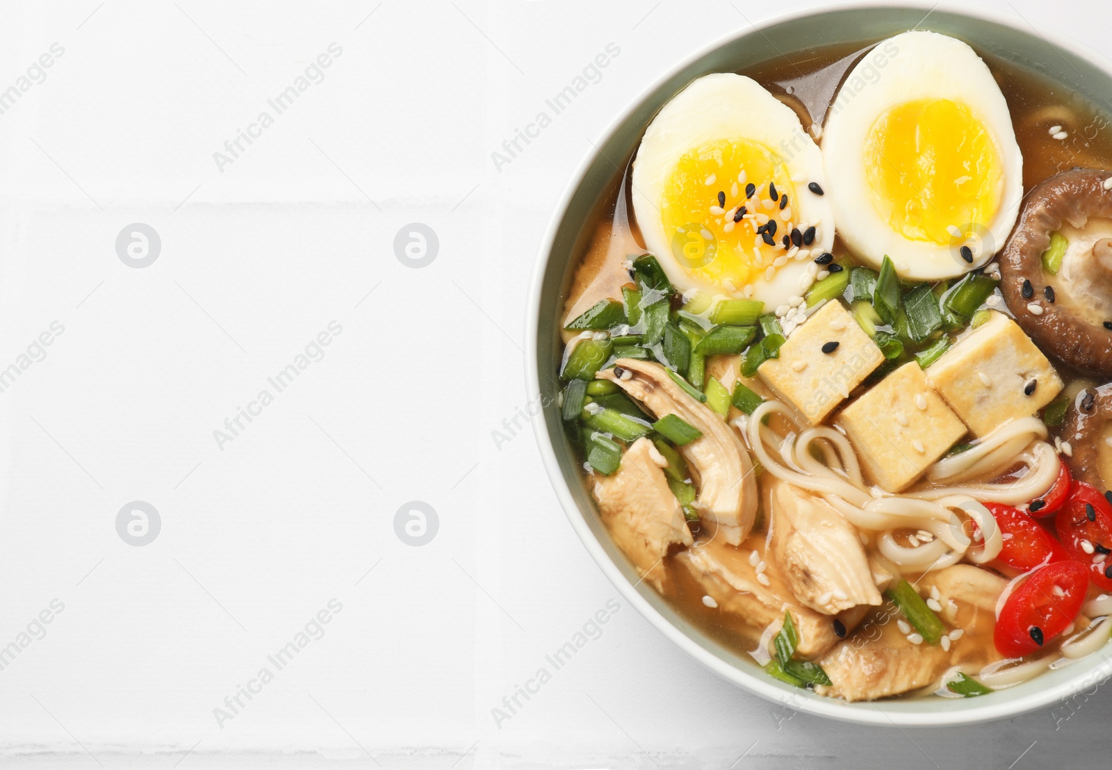 Photo of Noodle soup. Bowl of delicious ramen on white tiled table, top view. Space for text