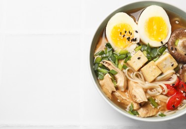 Noodle soup. Bowl of delicious ramen on white tiled table, top view. Space for text