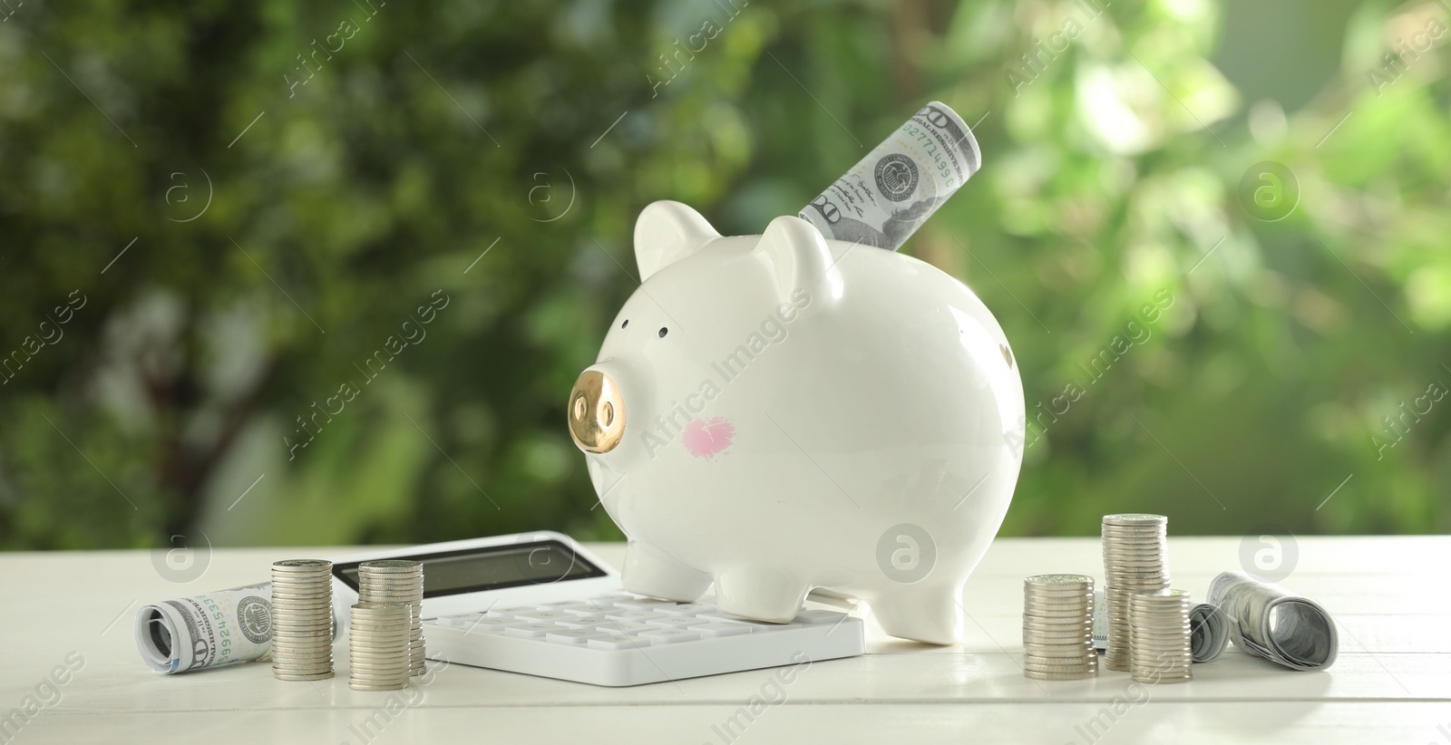 Photo of Financial savings. Piggy bank with dollar banknotes, stacked coins and calculator on white wooden table outdoors
