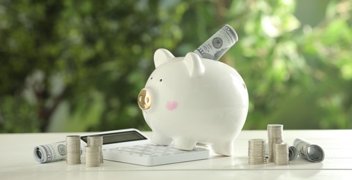 Financial savings. Piggy bank with dollar banknotes, stacked coins and calculator on white wooden table outdoors