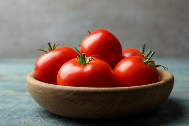 Photo of Ripe tomatoes in bowl on blue wooden table, closeup