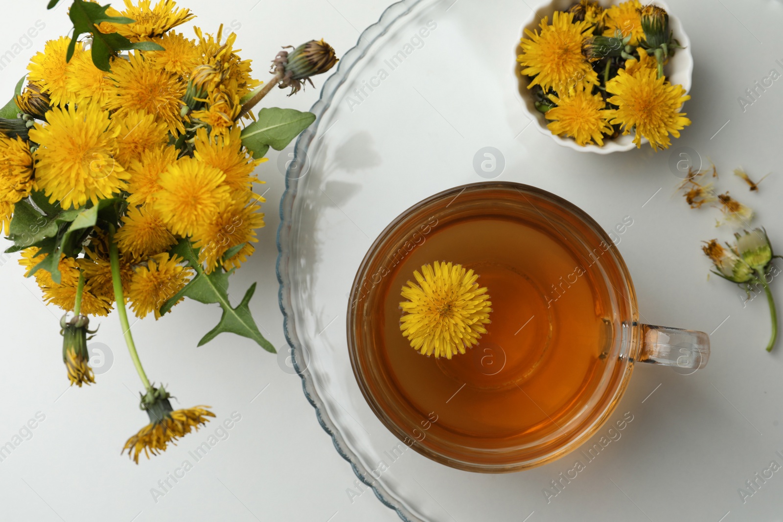 Photo of Delicious fresh tea and beautiful dandelion bouquet on white table, flat lay