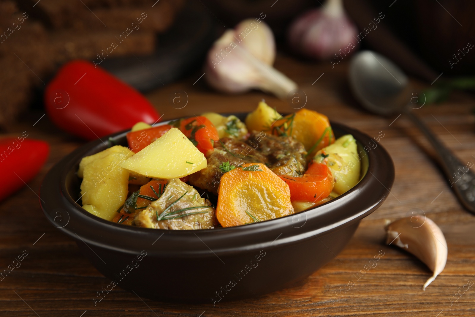 Photo of Tasty cooked dish with potatoes in earthenware on wooden table