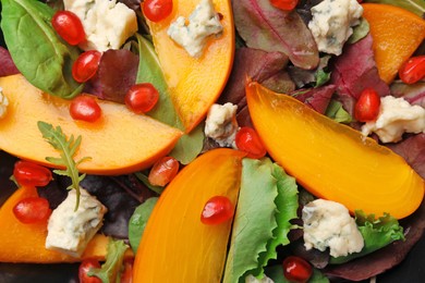 Photo of Delicious persimmon salad with cheese, pomegranate and spinach as background, closeup