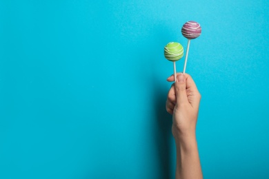 Woman holding bright delicious cake pops on color background, closeup. Space for text