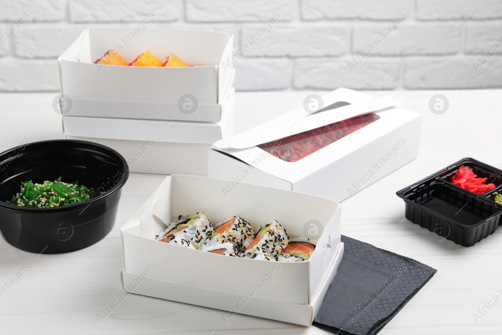 Photo of Food delivery. Paper boxes with delicious sushi rolls on white wooden table