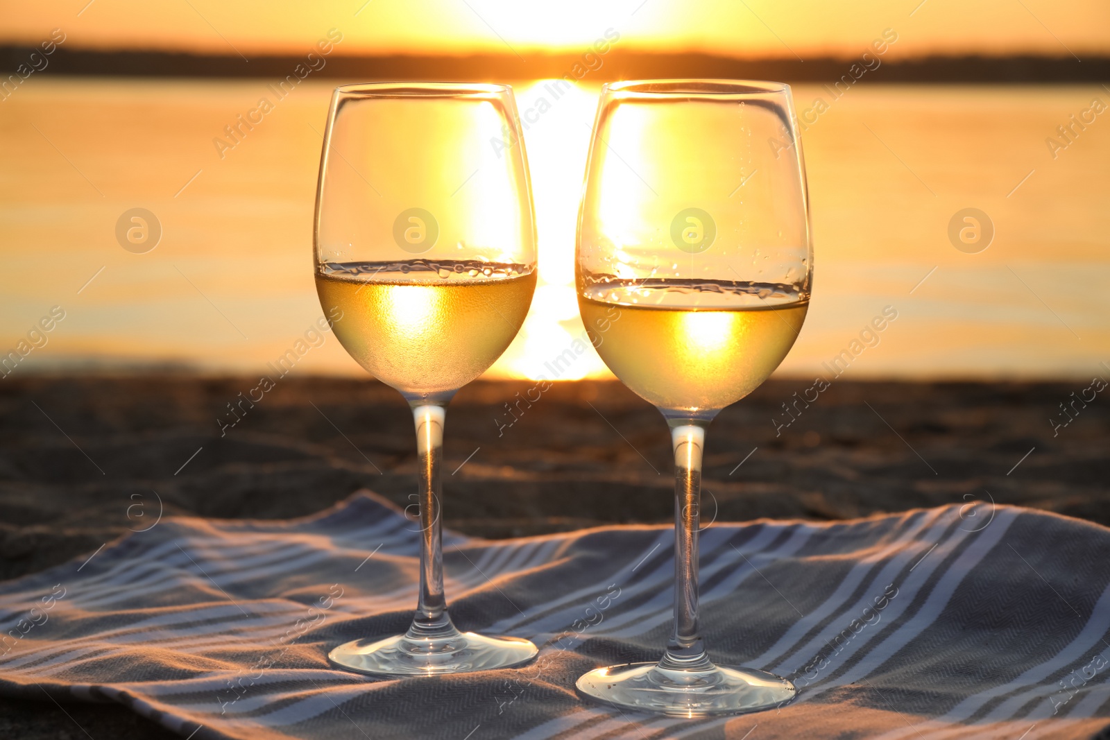 Photo of Glasses of delicious wine on riverside at sunset