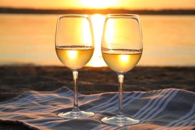 Glasses of delicious wine on riverside at sunset