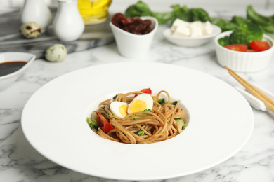 Photo of Tasty buckwheat noodles served on white marble table