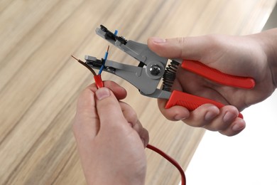 Photo of Professional electrician stripping wiring at wooden table, top view