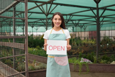 Female business owner holding OPEN sign in greenhouse