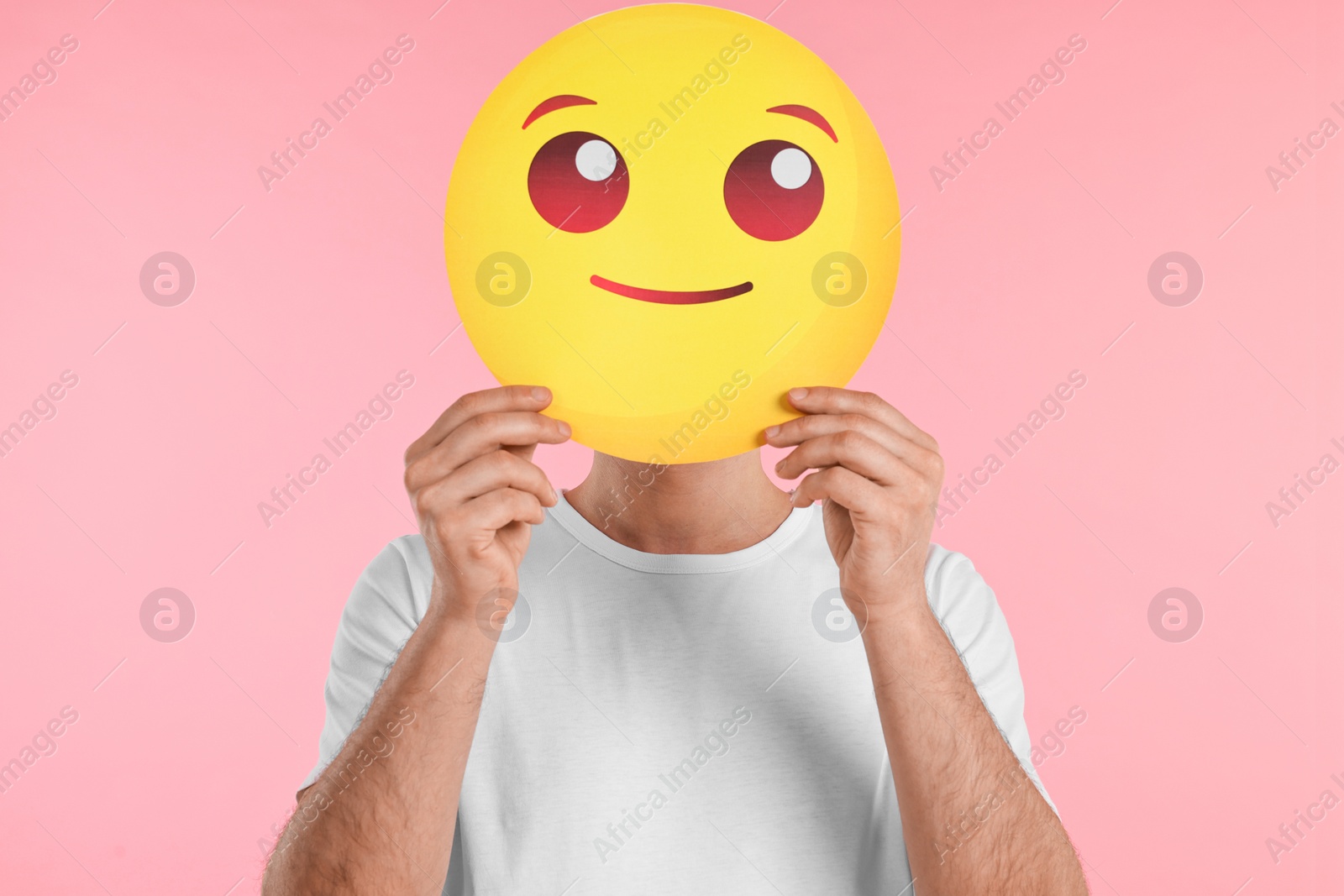 Photo of Man covering face with smiling emoticon on pink background