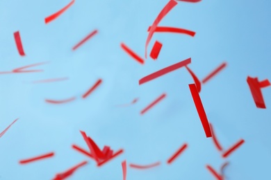 Photo of Shiny red confetti falling down on light blue background